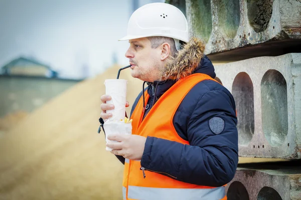 Trabajador bebiendo refrescos y comiendo papas fritas en el sitio de construcción — Foto de Stock