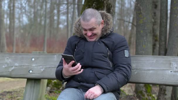 Счастливый человек с планшетным ПК смеется в парке на скамейке — стоковое видео