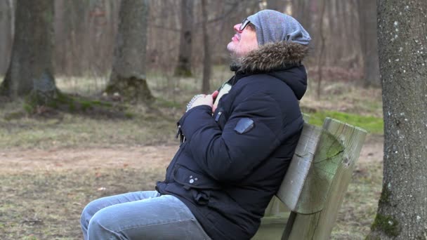 Muž s Bibli a růženec se modlí na lavičce v parku — Stock video