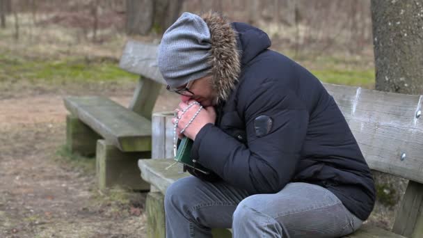 Uomo con Bibbia e rosario sulla panchina del parco — Video Stock