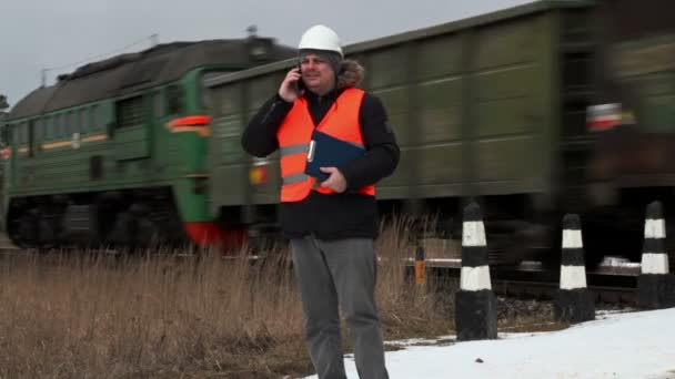 Robotnik pracujący na kolei rozmawia inteligentny telefon w pobliżu przejazdu kolejowego — Wideo stockowe