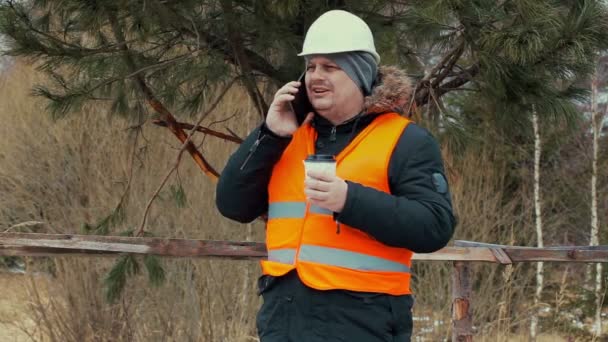 Forest werknemer met koffie en smartphones in de buurt van juniper — Stockvideo