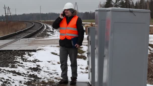 Работник железной дороги разговаривает по мобильному телефону возле электрокорпуса — стоковое видео