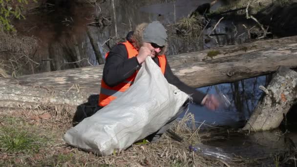 Man met de tas halen van lege plastic flessen in de buurt van rivier — Stockvideo