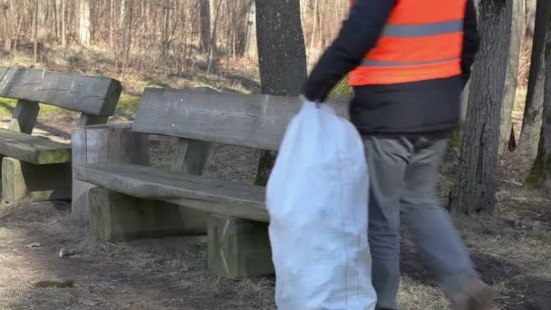 Мужчина проверяет пакет пластиковых бутылок на скамейке в парке — стоковое видео