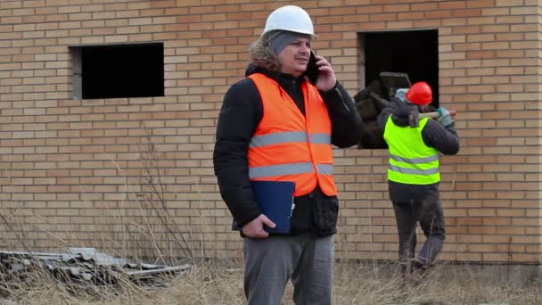 Menedżer witryny mówić na silny telefon i pracownik z młotem w pobliżu deski — Wideo stockowe