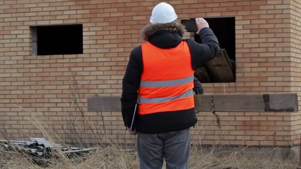 Bauleiter mit Tablet-PC gefilmt und Arbeiter trägt Brett — Stockvideo