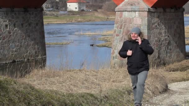 Hombre hablando por teléfono inteligente cerca de puente — Vídeo de stock
