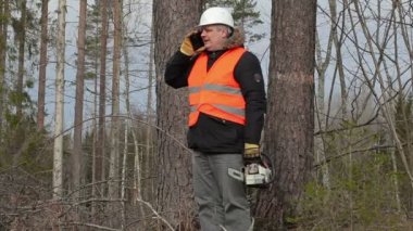 Oduncu tree yakınındaki akıllı telefonda konuşurken chainsaw ile 