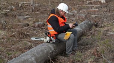 Ağacın üzerinde oturan ve tablet Pc kullanma chainsaw ile oduncu