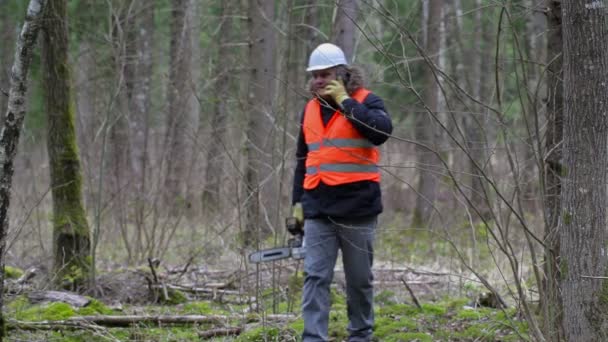 Lumberjack com motosserra e telefone inteligente na floresta — Vídeo de Stock
