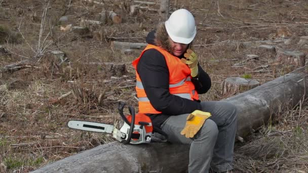 Lumberjack sitting on tree near chainsaw and using tablet PC — Stock Video