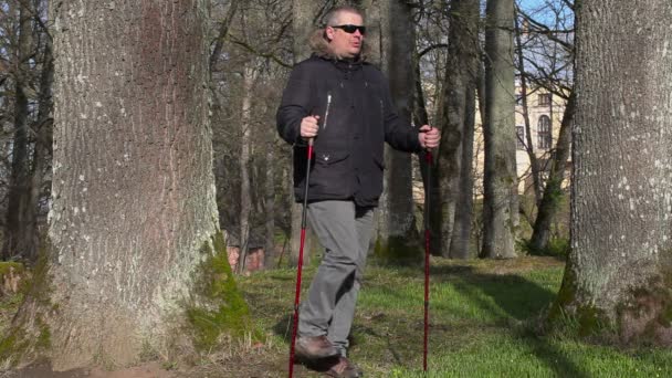 Турист с тросточками согревается в парке — стоковое видео