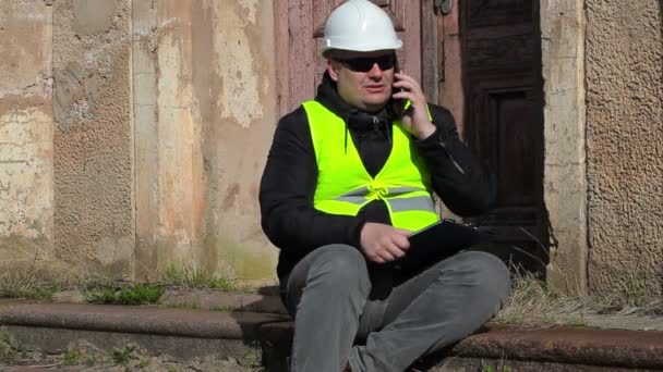 Злой инспектор здания сидит и разговаривает по смартфону — стоковое видео