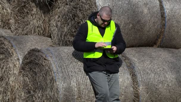 Agricultor usando tablet PC perto dos fardos de feno — Vídeo de Stock