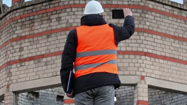 Инженер-строитель фотографирует на планшете рядом со зданием — стоковое видео