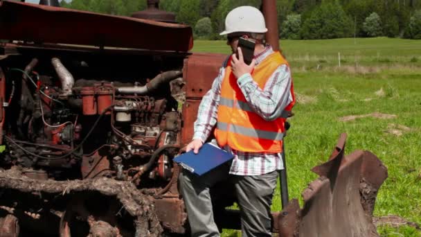 Trabalhador falando no telefone inteligente perto bulldozer quebrado — Vídeo de Stock