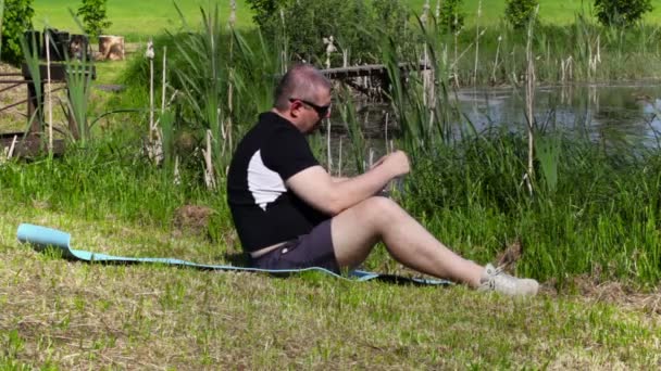 Homem falando no telefone inteligente e relaxar perto do lago — Vídeo de Stock