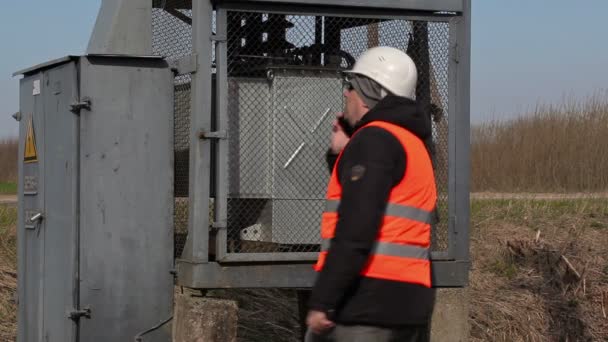 Electricista hablando por teléfono inteligente cerca del transformador — Vídeo de stock