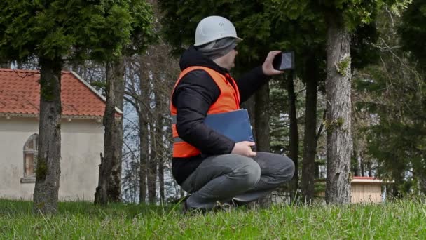 Byggnaden inspektören ta bilder på tablet Pc nära träd — Stockvideo