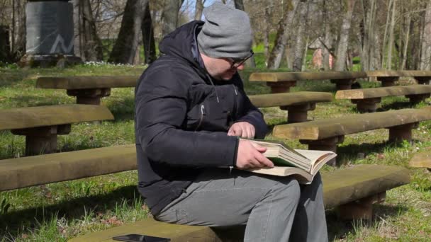 Man läsa två böcker på bänk i parken — Stockvideo