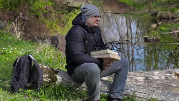 Man med två böcker avkopplande i äng nära floden — Stockvideo