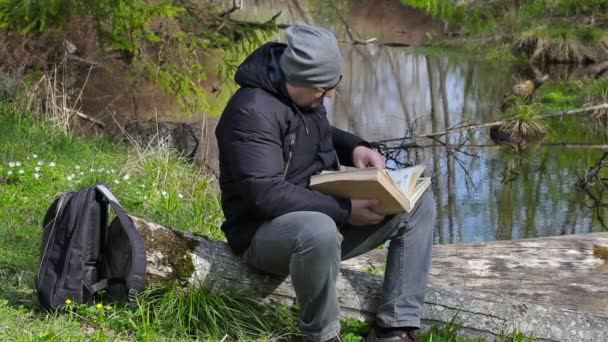 Hombre leyendo libro en prado cerca de río — Vídeo de stock