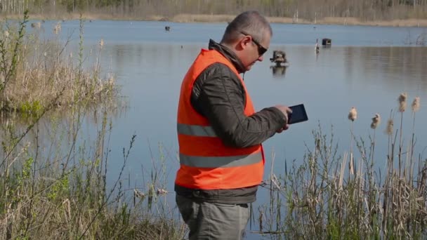 Орнітолог використовує планшетний ПК біля будинків качки біля озера — стокове відео