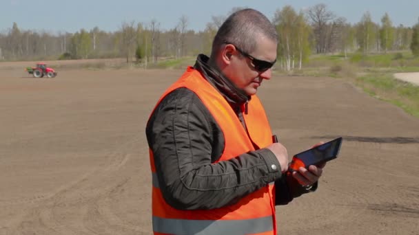 Bonde med hjälp av tablet Pc på fältet där traktorn harrow marken — Stockvideo