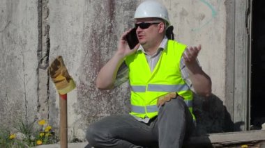 Akıllı telefon duvarının yakınında konuşurken sinirli inşaat işçisi 