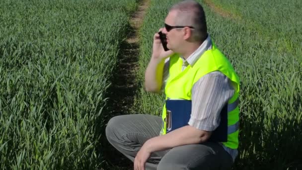 Фермер со смартфоном и папкой на зеленом зерновом поле — стоковое видео