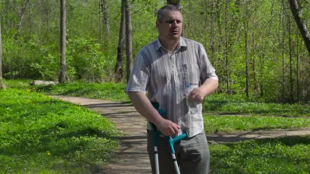 Людина з обмеженими можливостями п'є воду в парку — стокове відео