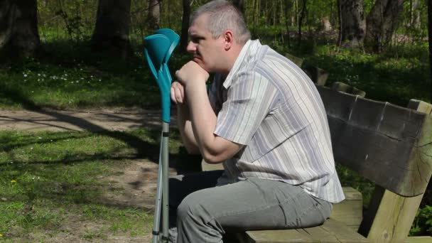 Deprimido deficiente homem com muletas no banco no parque — Vídeo de Stock