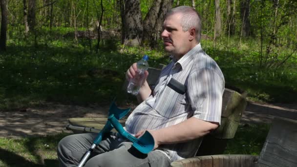 Homem com deficiência com muletas sentado no banco e água potável — Vídeo de Stock