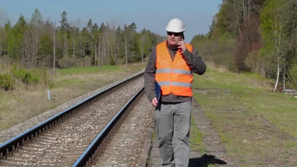 Robotnik pracujący na kolei chodzenia i mówienia na inteligentnego telefonu w pobliżu kolejowego — Wideo stockowe