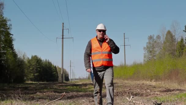 Elektryk rozmawia inteligentny telefon i sprawdzić stan techniczny linii wysokiego napięcia — Wideo stockowe