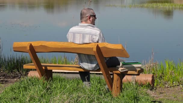 Man talking on smart phone on the bench near river — Stock Video