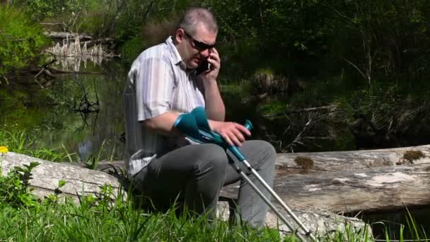 Zdravotně postižený muž s berlemi, mluví na smartphonu poblíž řeky — Stock video