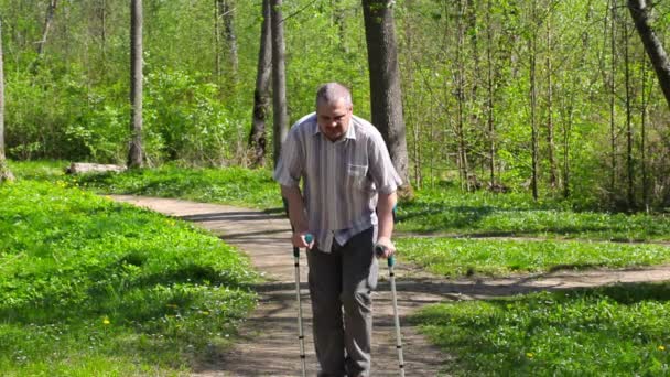 Уставший инвалид с костылями прогуливается по парку — стоковое видео