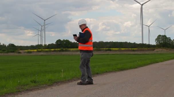 Ingeniero electricista caminando y tomar fotos en el teléfono inteligente cerca de molinos de viento — Vídeo de stock