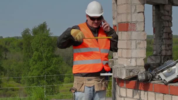 Construtor falando no telefone inteligente e usando fita métrica — Vídeo de Stock