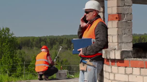 Construtor usando telefone inteligente perto do edifício — Vídeo de Stock