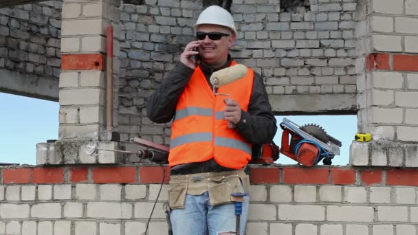Constructor con rodillo de pintura hablando en el teléfono inteligente — Vídeos de Stock