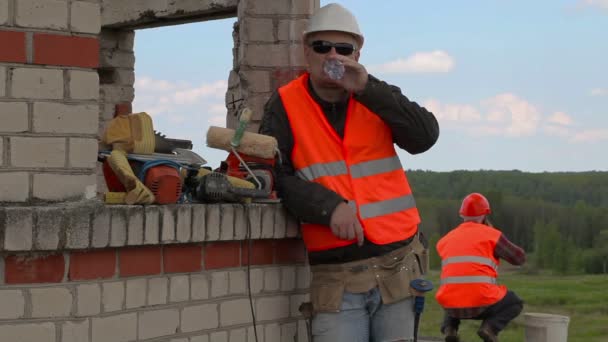 Builder drinking water near unfinished building — Stock Video