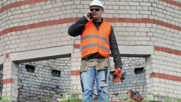 Construtor falando no telefone inteligente e andando perto do edifício — Vídeo de Stock