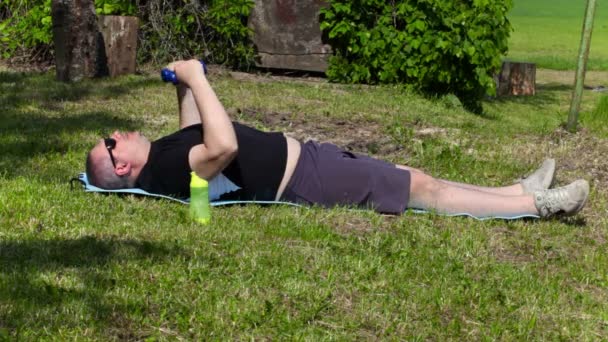 Мужчина с избыточным весом делает упражнения с гантелями на outddor летом — стоковое видео