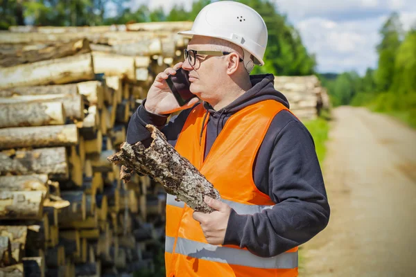 Holzfäller mit Baumrinde und Smartphone in der Nähe von Holzstapel — Stockfoto