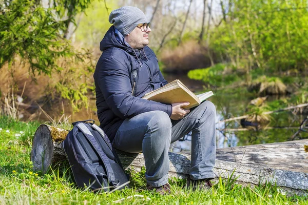 Homme lisant un livre dans un pré près d'une rivière — Photo