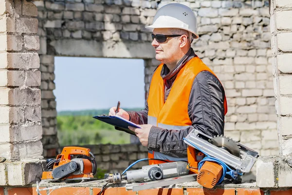 Pracownik budowlany, pisanie w pobliżu narzędzia w niedokończony budynek — Zdjęcie stockowe