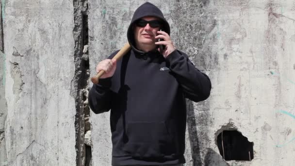 Homem com um bastão de beisebol falando no telefone inteligente — Vídeo de Stock